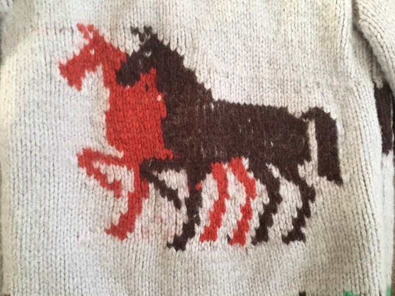 May include: A white knitted sweater with a brown and red knitted horse design.