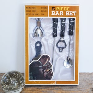 Könnte beinhalten: Ein Vintage-Bar-Set mit 6 Teilen in einer braunen und weißen Box. Das Set enthält einen Rührlöffel, ein Sieb, einen Doppel-Jigger, ein Bar-Zubehör, einen Flaschen-/Dosenöffner und einen Zahnstocher.