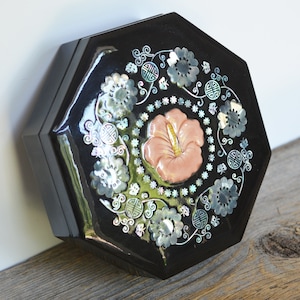 May include: Octagonal black lacquered box with intricate floral designs and a pink flower inlay. The box is decorated with mother-of-pearl accents.