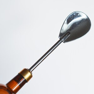 May include: A silver bottle stopper with a long, thin handle and a rounded, spoon-shaped end.