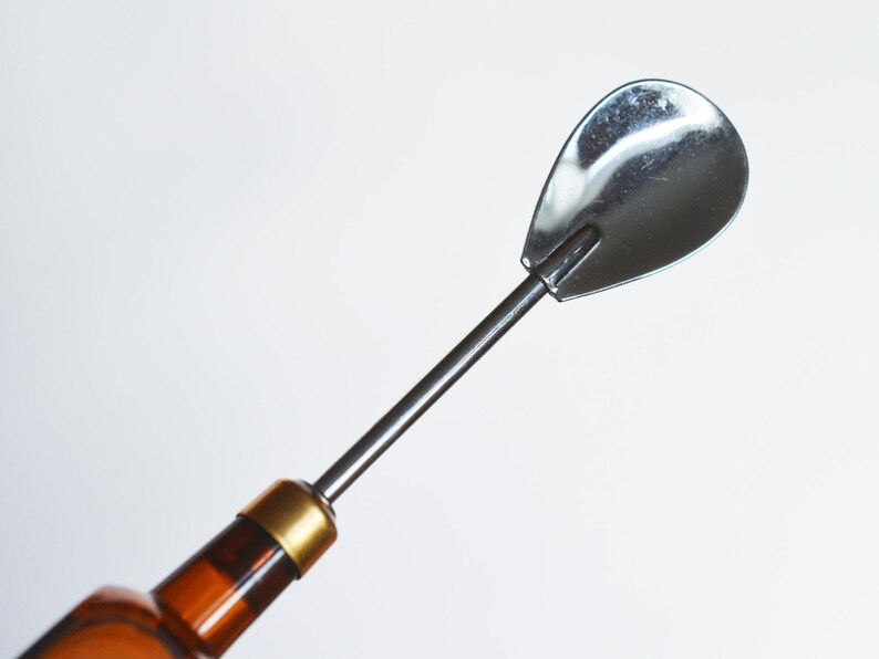 May include: A silver bottle stopper with a long, thin handle and a rounded, spoon-shaped end.
