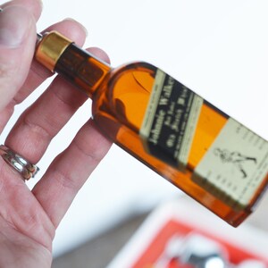 May include: A miniature glass bottle shaped like a bottle of Johnnie Walker Scotch whisky. The bottle is brown and has a gold cap. The label reads "Johnnie Walker Old Scotch Whisky".