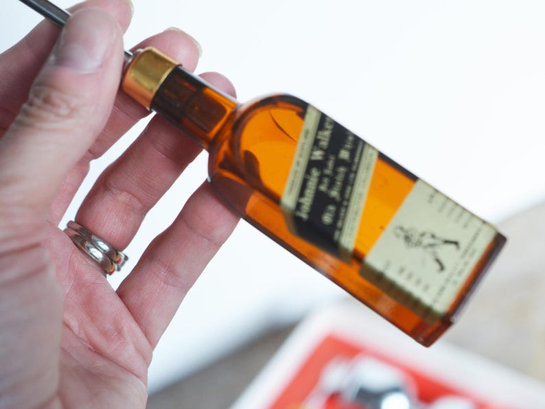 May include: A miniature glass bottle shaped like a bottle of Johnnie Walker Scotch whisky. The bottle is brown and has a gold cap. The label reads "Johnnie Walker Old Scotch Whisky".