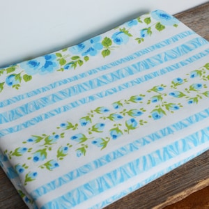 May include: White fabric with blue and green floral pattern. The fabric has blue and white stripes with a zig-zag pattern.