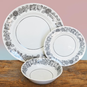 May include: A set of three white ceramic plates with black floral designs. The plates are nested together, with the largest plate on the bottom and the smallest plate on top. The plates have a simple, elegant design.