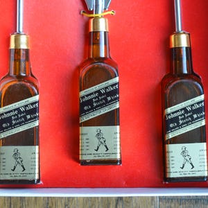 May include: Three miniature bottles of Johnnie Walker Red Label Old Scotch Whisky. The bottles are clear glass with black labels and gold accents. The labels feature the Johnnie Walker logo and text.