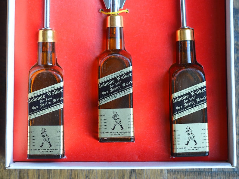 May include: Three miniature bottles of Johnnie Walker Red Label Old Scotch Whisky. The bottles are clear glass with black labels and gold accents. The labels feature the Johnnie Walker logo and text.