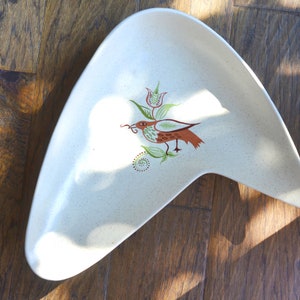 May include: A white ceramic serving dish in the shape of a boomerang with a brown bird and green floral design.