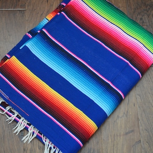 May include: A colorful Mexican blanket with stripes of blue, red, yellow, green, and pink. The blanket is folded and has fringe on the edges.