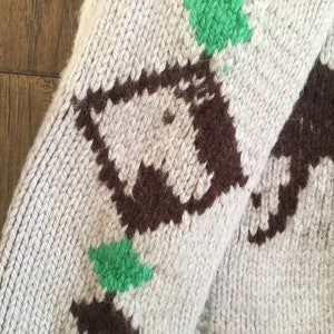 May include: A close-up of a knitted sweater with a brown and green pattern. The sweater is made of a soft, fuzzy material and has a relaxed fit.