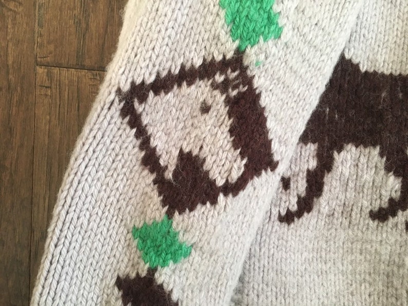 May include: A close-up of a knitted sweater with a brown and green pattern. The sweater is made of a soft, fuzzy material and has a relaxed fit.