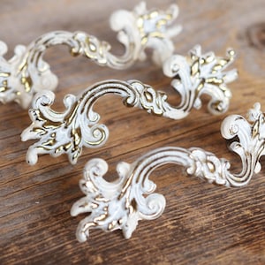 May include: Four ornate white and gold cabinet pulls with a floral design.