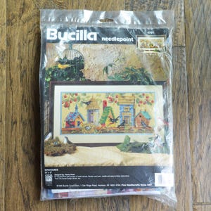 May include: A Bucilla needlepoint kit featuring a colorful design of birdhouses with birds and flowers. The kit includes a 12-inch by 17-inch canvas, yarn, needle, and instructions. The kit is labeled "Birdhouses" and "4701".