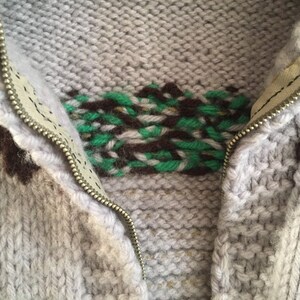 May include: A close-up of a gray knitted sweater with a zipper and a brown and green geometric pattern.