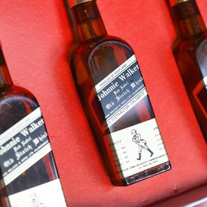 May include: Three miniature bottles of Johnnie Walker Red Label Scotch Whisky. The bottles are brown glass with a gold label and black text. The label says "Johnnie Walker Red Label Old Scotch Whisky" and "Produce of Scotland".