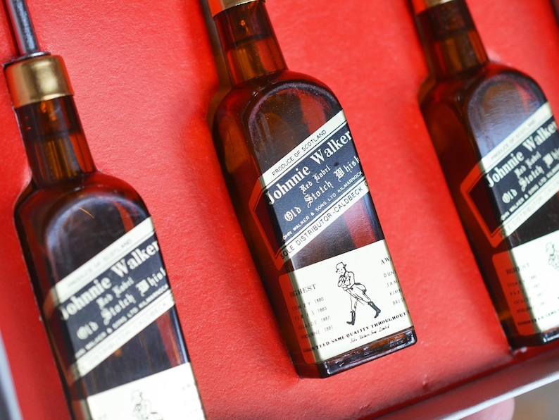 May include: Three miniature bottles of Johnnie Walker Red Label Scotch Whisky. The bottles are brown glass with a gold label and black text. The label says "Johnnie Walker Red Label Old Scotch Whisky" and "Produce of Scotland".