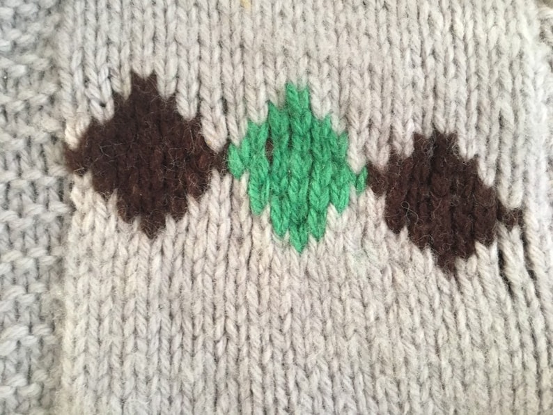 May include: Close-up of a knitted fabric with a brown and green diamond pattern. The fabric is a light gray color.