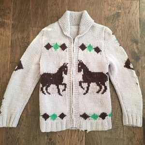May include: A light purple knitted cardigan with a zipper closure. The cardigan features a brown and green horse design.