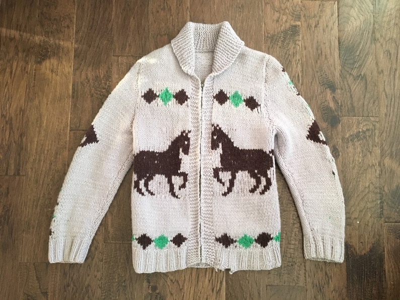 May include: A light purple knitted cardigan with a zipper closure. The cardigan features a brown and green horse design.