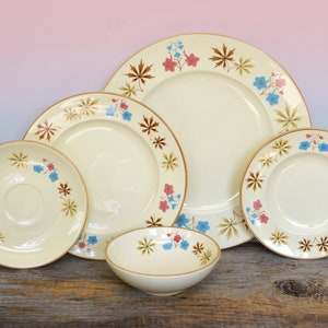 May include: Set of four vintage ceramic plates with a floral design. The plates feature a cream background with brown, pink, and blue floral accents. The plates are arranged in a nested pattern, with the largest plate at the bottom and the smallest plate at the top.