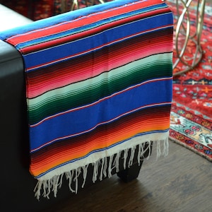May include: A colorful striped Mexican blanket with white fringe, draped over a black leather couch.