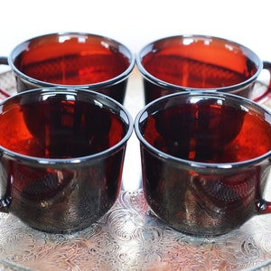 Può includere: Quattro tazze da tè in vetro rosso scuro con manici su un vassoio d'argento con un design ornamentale.
