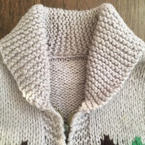 May include: A gray knitted cardigan with a zipper closure and a large collar. The cardigan has a geometric pattern in green, brown, and white.