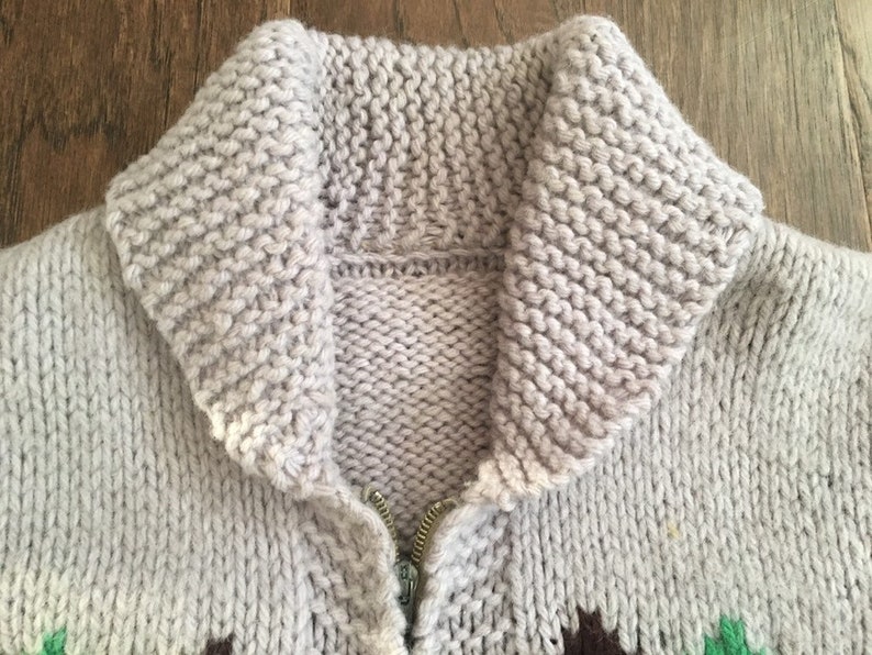 May include: A gray knitted cardigan with a zipper closure and a large collar. The cardigan has a geometric pattern in green, brown, and white.