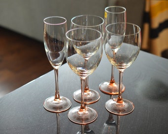 May include: Five clear glass wine glasses with a pink rim on a black surface. The glasses are empty and are arranged in a semi-circle.