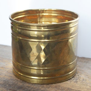 Puede incluir: Un macetero de metal dorado con un patrón de diamante. El macetero es redondo y tiene un acabado liso y brillante.