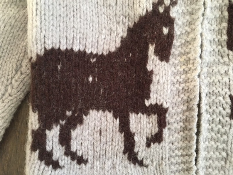 May include: A knitted cardigan with a brown unicorn design. The cardigan is made of a soft, fluffy yarn.