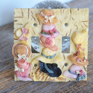 May include: A decorative light switch cover with a yellow background and a design of stacked hats in various colors and patterns.