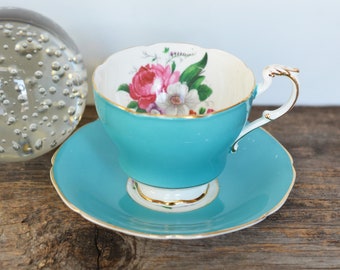 May include: A turquoise teacup and saucer set with a floral pattern. The cup has a gold rim and a delicate handle. The saucer is also turquoise with a gold rim.