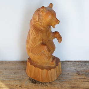 May include: A wooden carving of a bear standing on a wooden base. The bear is carved in a realistic style and has a brown color.