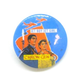 Op de afbeelding: Een ronde, blauwe button met een retro illustratie. De button toont twee figuren, een speer en oranje vliegtuigen. Tekst bevat "JET BOY JET GIRL" en "CHRON GEN".