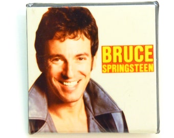 May include: A yellow and orange CD case with a photo of Bruce Springsteen on the front. The text "BRUCE SPRINGSTEEN" is printed in yellow on the case.