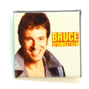 May include: A yellow and orange CD case with a photo of Bruce Springsteen on the front. The text "BRUCE SPRINGSTEEN" is printed in yellow on the case.