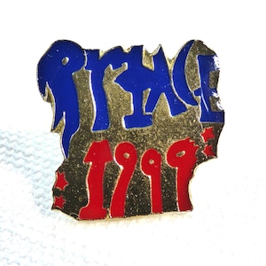 May include: A rectangular pin with the word "PRIDE" in blue letters over the year "1999" in red. The pin has a gold border and small red stars. The background is white.