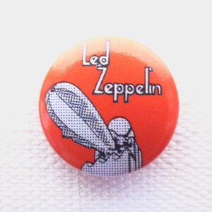 May include: A round, orange button with a black and white image of a blimp and the text "Led Zeppelin" in black.