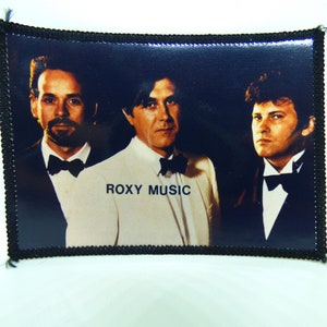 Op de afbeelding: Een zwart-witfoto van drie mannen in pak en vlinderdas. De mannen zijn in een band genaamd "ROXY MUSIC".