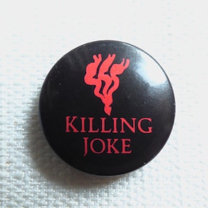 Puede incluir: Un botón negro con un símbolo rojo en forma de corazón y el texto "KILLING JOKE" en rojo.