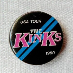 Könnte beinhalten: Ein schwarzer und blauer Knopf mit dem Text "USA Tour The Kinks 1980" in weißer und rosa Schrift.