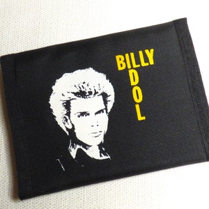 Puede incluir: Cartera negra con una imagen blanca de Billy Idol y el texto "BILLY DOL" en amarillo.
