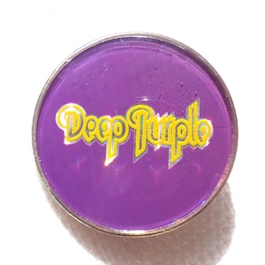 Op de afbeelding: Een ronde pin met een glanzende paarse achtergrond en een zilverkleurige metalen rand. De tekst Deep Purple staat in het midden in een gestileerd geel lettertype met een dunne zilveren omlijning, wat een levendig contrast geeft met het paars.