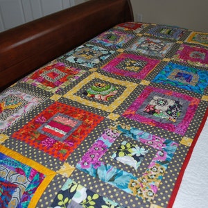 May include: A colorful patchwork quilt with a gray polka dot background. The quilt features square blocks in various colors, including pink, blue, orange, and yellow, with floral and patterned fabrics. A red border frames the quilt.