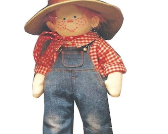 May include: A handmade doll wearing a red and white checkered shirt, blue overalls, and a brown hat. The doll has red hair and freckles.