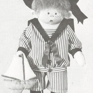 May include: A black and white striped sailor outfit with a black sailor hat and a white sailboat. The doll is made of fabric and has a red nose and black eyes.