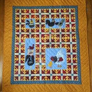 May include: A quilted wall hanging with a yellow border and a blue and white center. The center features a patchwork design with various geometric shapes and a repeating pattern of chickens. The chickens are in various colors, including red, black, and white.