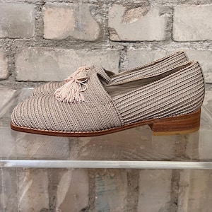Könnte beinhalten: Beigefarbene Strick-Slipper mit einem rosa Quasten und einem Holzabsatz.