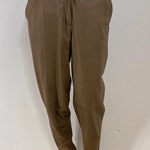 Puede incluir: Pantalones marrones con un patrón texturizado que recuerda a la piel de serpiente. Estos pantalones presentan un diseño de cintura alta con cierre de cremallera frontal, trabillas para cinturón y bolsillos laterales. Las piernas son estrechas.